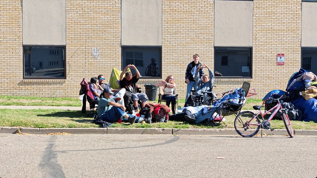 Members of a homeless encampment pose together and make heart shapes with their hands.